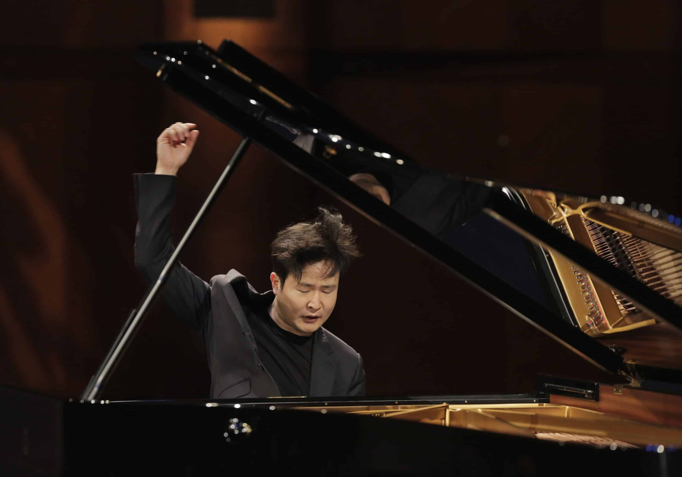 Yekwon Sunwoo expressively playing the piano with his hand up in the air.